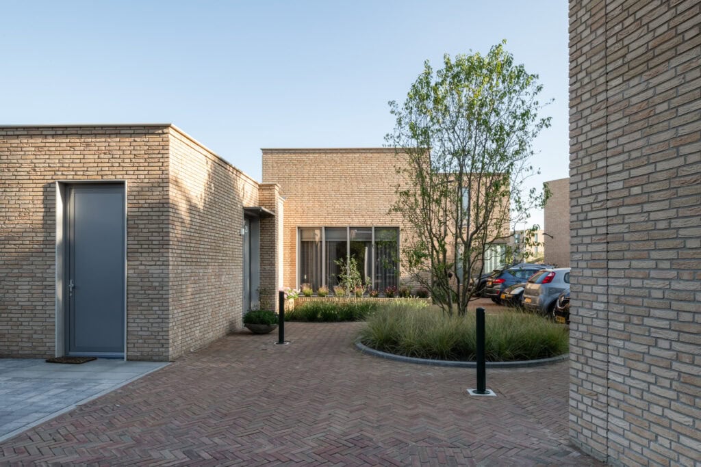 Modern architectuur woning met strakke bakstenen gevel en groene tuin, rustige woonomgeving in Nederland, duurzame bouwstijl, ruime parkeerplaatsen, geïnspireerd door studio redd.