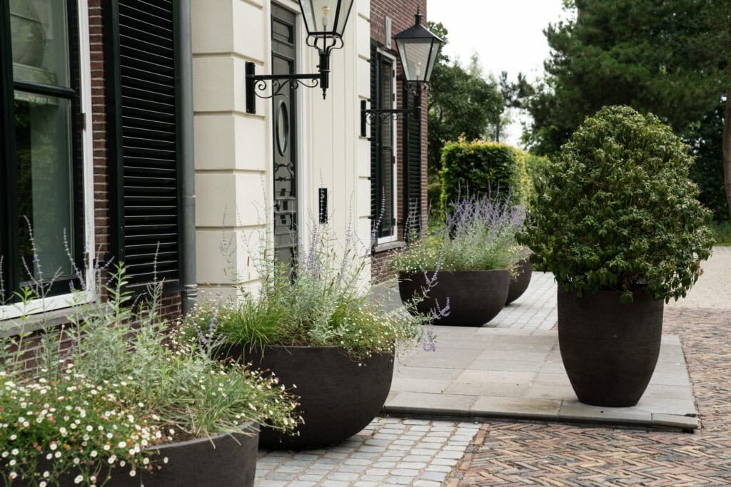 Rustieke buitenboordversiering met grote zwarte plantenpotten en bloemrijke tuin voor stijlvolle tuinontwerp en terrasdecoratie.