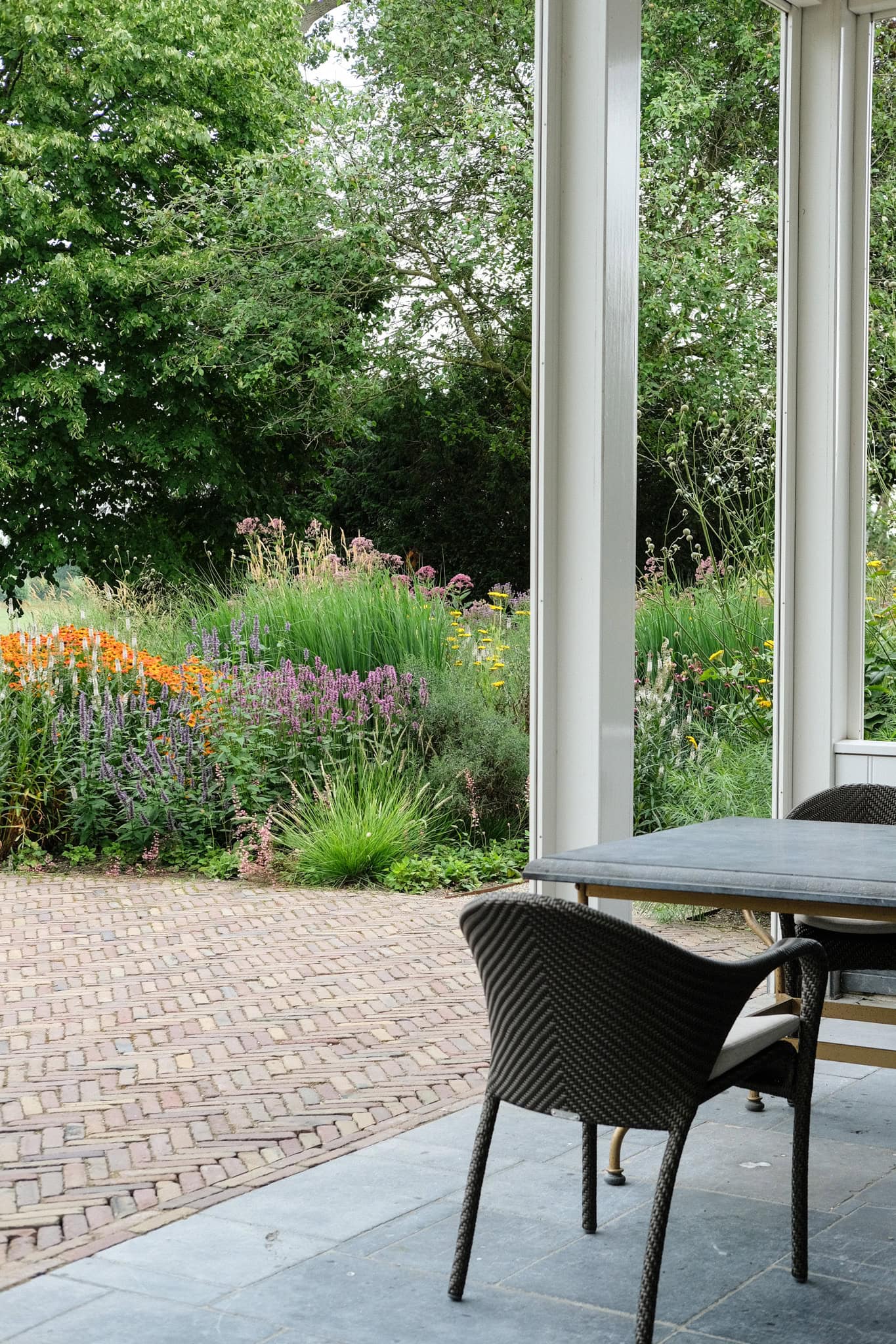 Rustig terras met uitzicht op kleurrijke tuin vol bloemen en groen, ideaal voor ontspanning en genieten van de natuur, ontworpen door Studio REDD.