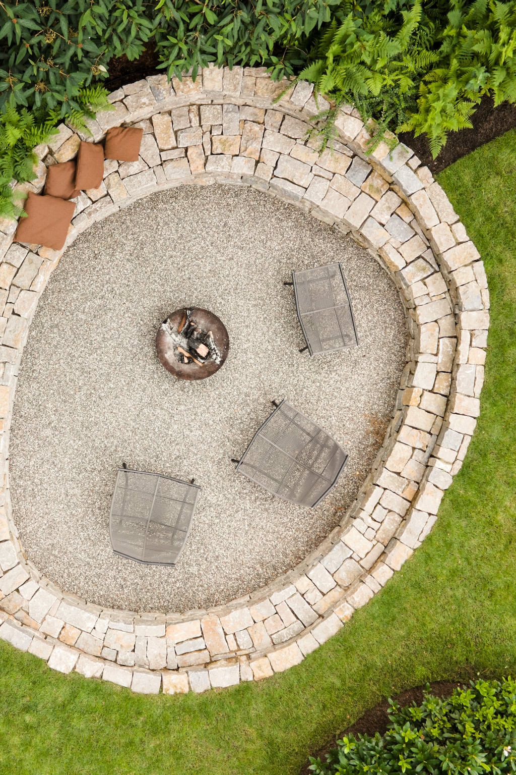 Sfeervolle tuin met rustiek stenen bloembed, comfortabele zitplaatsen en een vuurplaats, perfect voor gezellig buitenleven en ontspanning in een groene omgeving.