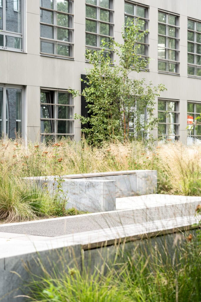 Moderne kantoorgevel met grote ramen, groene tuin en waterpartij, ontworpen voor een duurzame en natuurlijke werkomgeving.