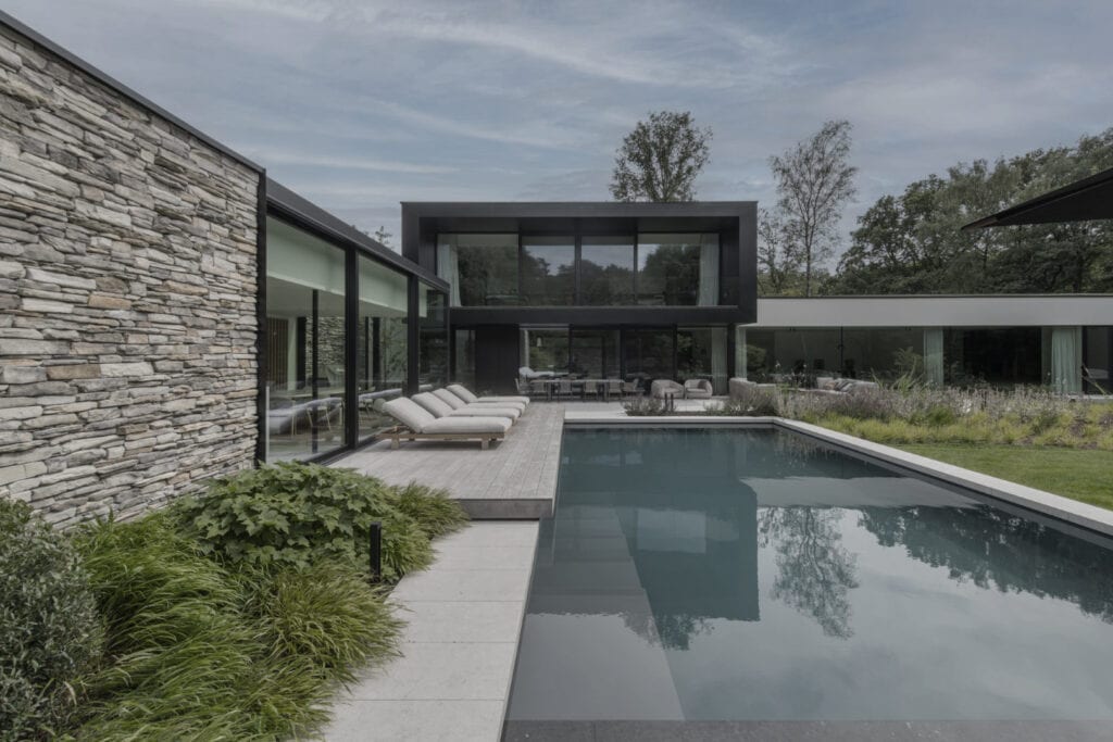 Moderne villa met zwembad, tuin en grote glazen ramen, ontworpen door Studio REDD, in een groene omgeving.