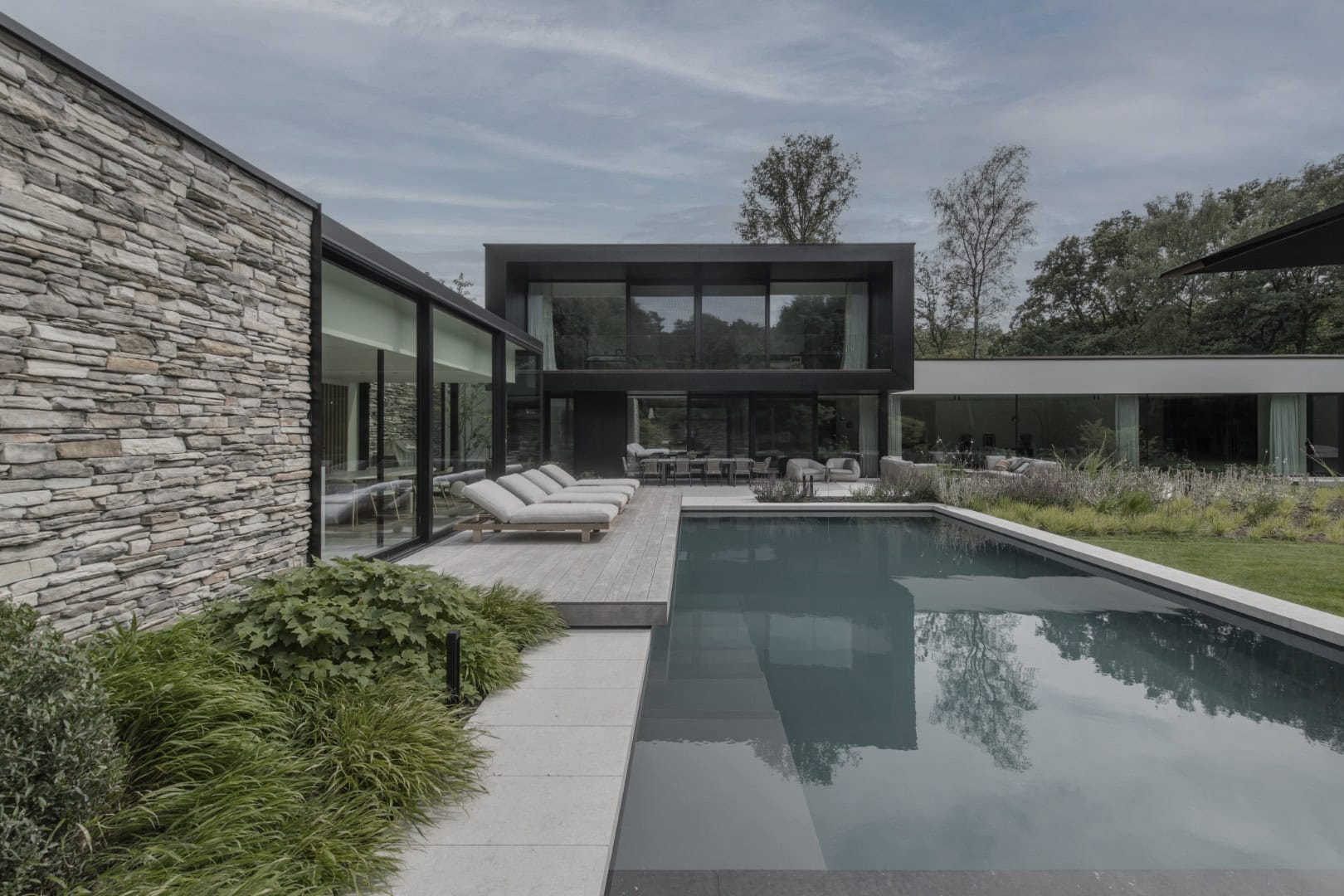 Moderne villa met zwembad, tuin en grote glazen ramen, ontworpen door Studio REDD, in een groene omgeving.