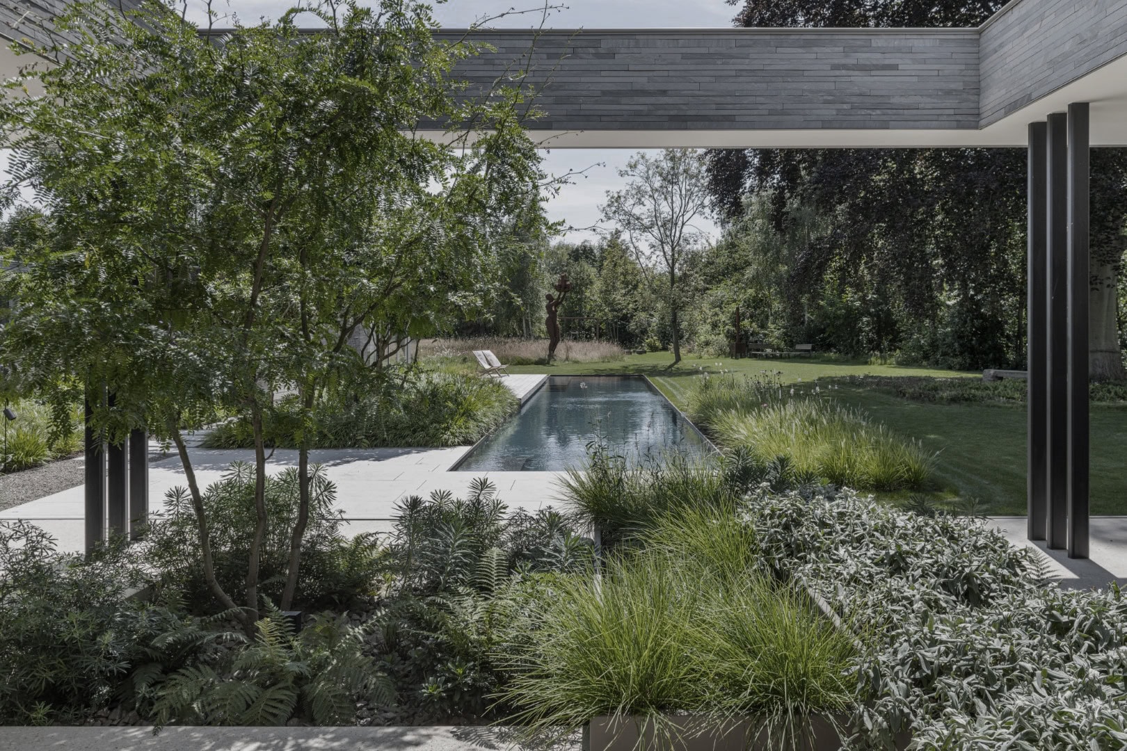 Moderne tuin met zwembad, omgeven door groen en bomen, ontworpen door Studio REDD voor een natuurlijke uitstraling.