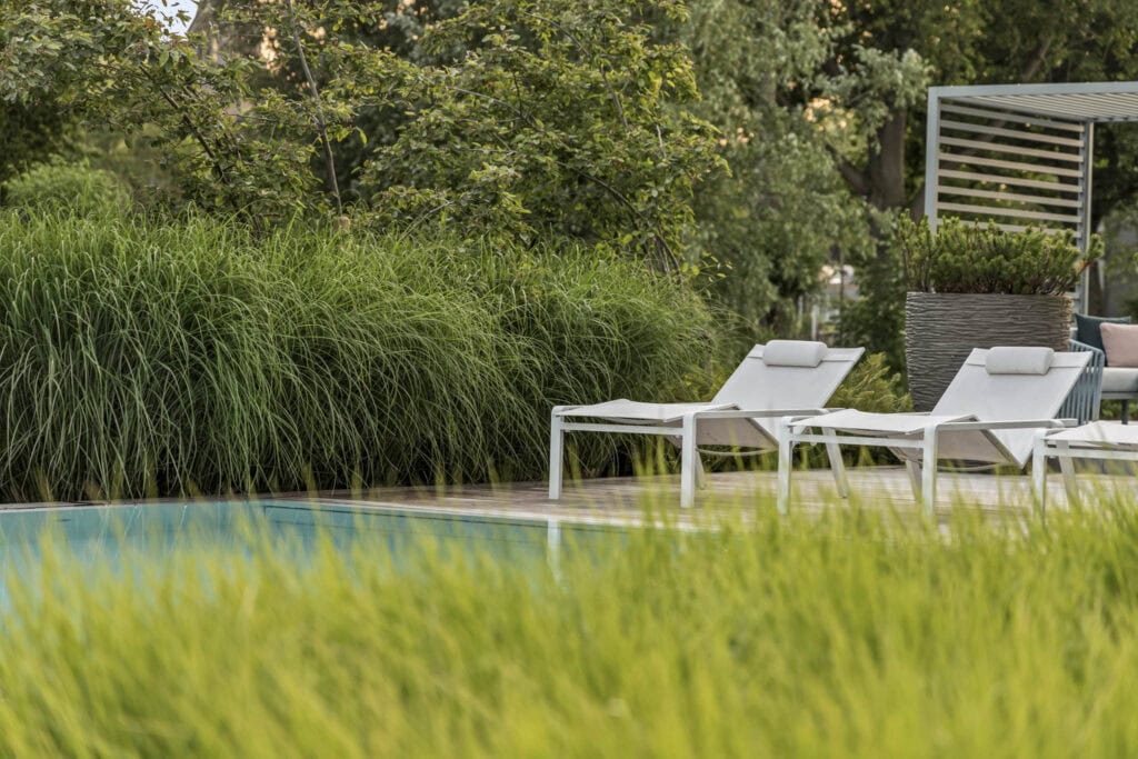 Twee witte lounge stoelen naast een zwembad in een groene tuin, perfect voor ontspanning en genieten van de buitenlucht.