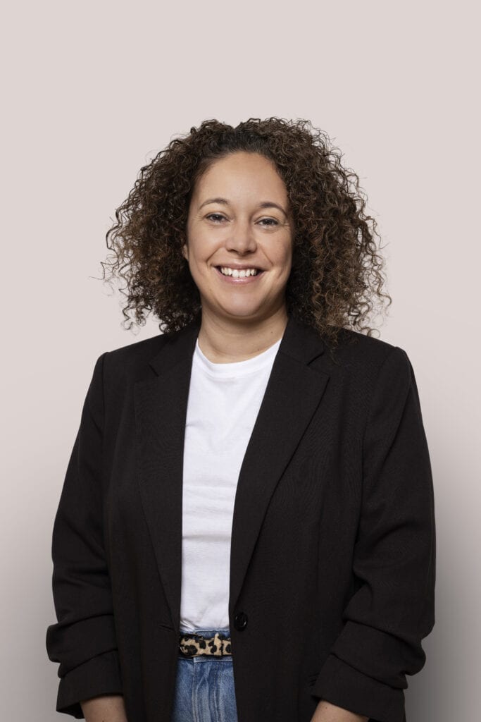 Vrouw met curly haar in zakelijke outfit, lachend voor een neutrale achtergrond, geschikt voor zakelijke en creatieve doeleinden.
